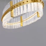 Lampa wisząca Mayo D90 w kolorze złotym, z jednym źródłem światła LED o mocy 45W. Okrągła konstrukcja z przezroczystymi elementami, w której widoczne są metalowe detale oraz dekoracyjne pręty szklane. Zawieszona pod kątem.