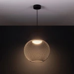 Czarna lampa wisząca Rita z siatkowym kloszem, źródło światła LED 19W, zawieszona na cienkim przewodzie. Klosz ma okrągły kształt, emitując ciepłe światło. Tło w ciemnym kolorze, podkreślające nowoczesny design.