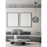 Lampa wisząca Rita w czarnym kolorze z metalowym kloszem w kształcie kuli, zawieszona na cienkim przewodzie. Widoczna w nowoczesnym wnętrzu z szaro-srebrną sofą, białymi dekoracjami na stole oraz pustymi ramkami na ścianie.