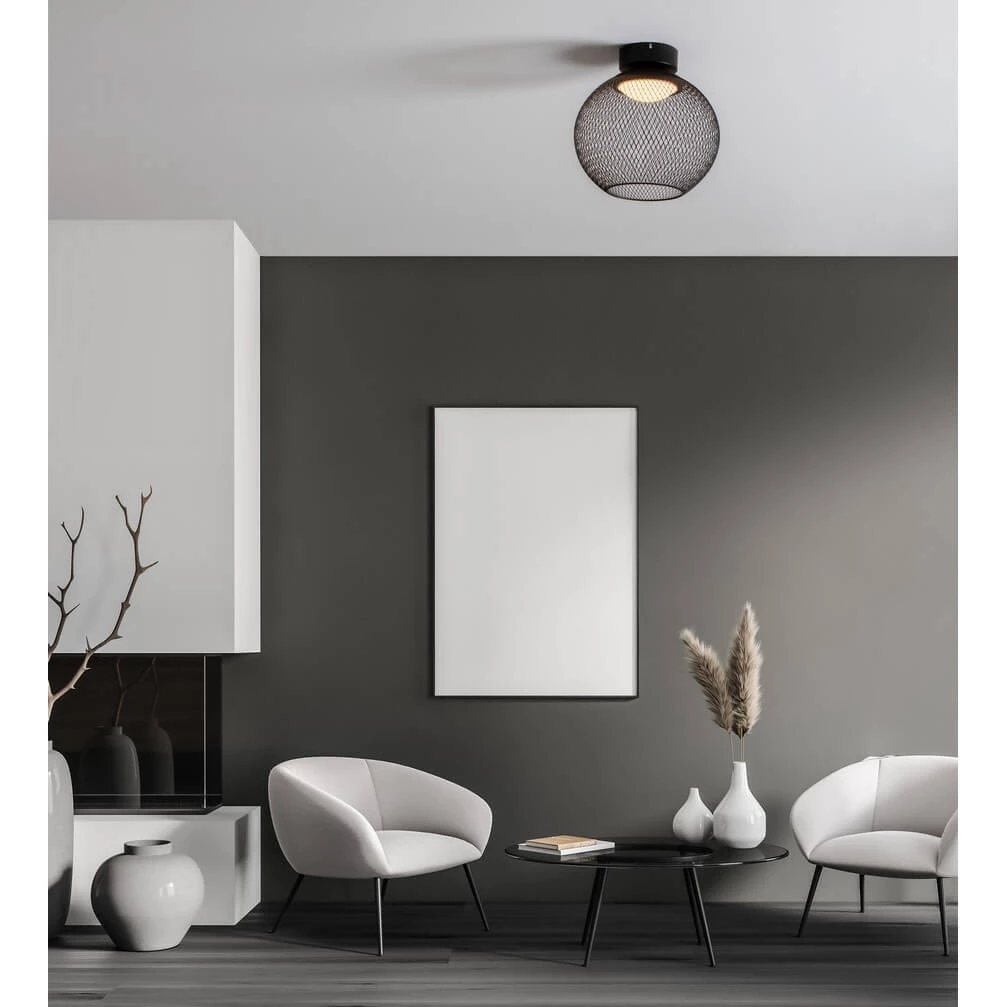 Czarna lampa sufitowa Rita z siatkowym kloszem, z zamontowanym źródłem światła LED 12W, wisząca na białym suficie. W tle nowoczesne wnętrze z jasnymi fotelami i czarnym stolikiem.