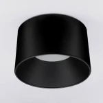Czarna lampa sufitowa LED Bajo o mocy 24W, o cylindrycznym kształcie, zamontowana na gładkim, jasnym tle. Widoczny otwór na źródło światła w centrum. Prosty, nowoczesny design.