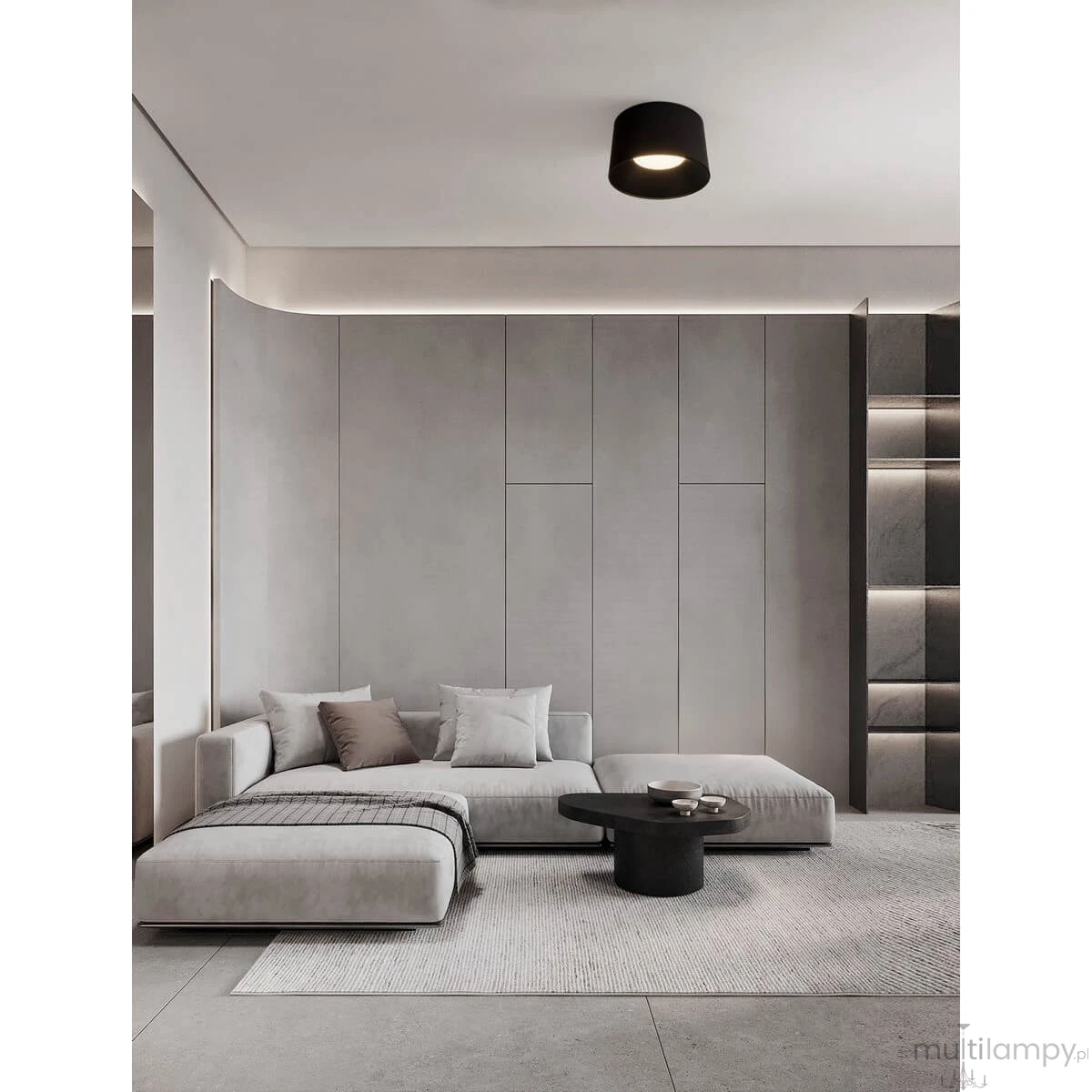 Czarna lampa sufitowa LED Bajo 35W w minimalistycznym stylu, zamontowana na jasnym suficie. W tle widoczna nowoczesna aranżacja wnętrza z szarym narożnikiem i okrągłym stolikiem. Oświetlenie tworzy przytulną atmosferę w przestrzeni.