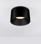 Czarna lampa sufitowa LED Bajo o mocy 35W, o cylindrycznym kształcie, zamontowana na suficie. Emituje ciepłe światło, z widocznym okrągłym kloszem i matowym wykończeniem. Prosta forma, idealna do nowoczesnych wnętrz.