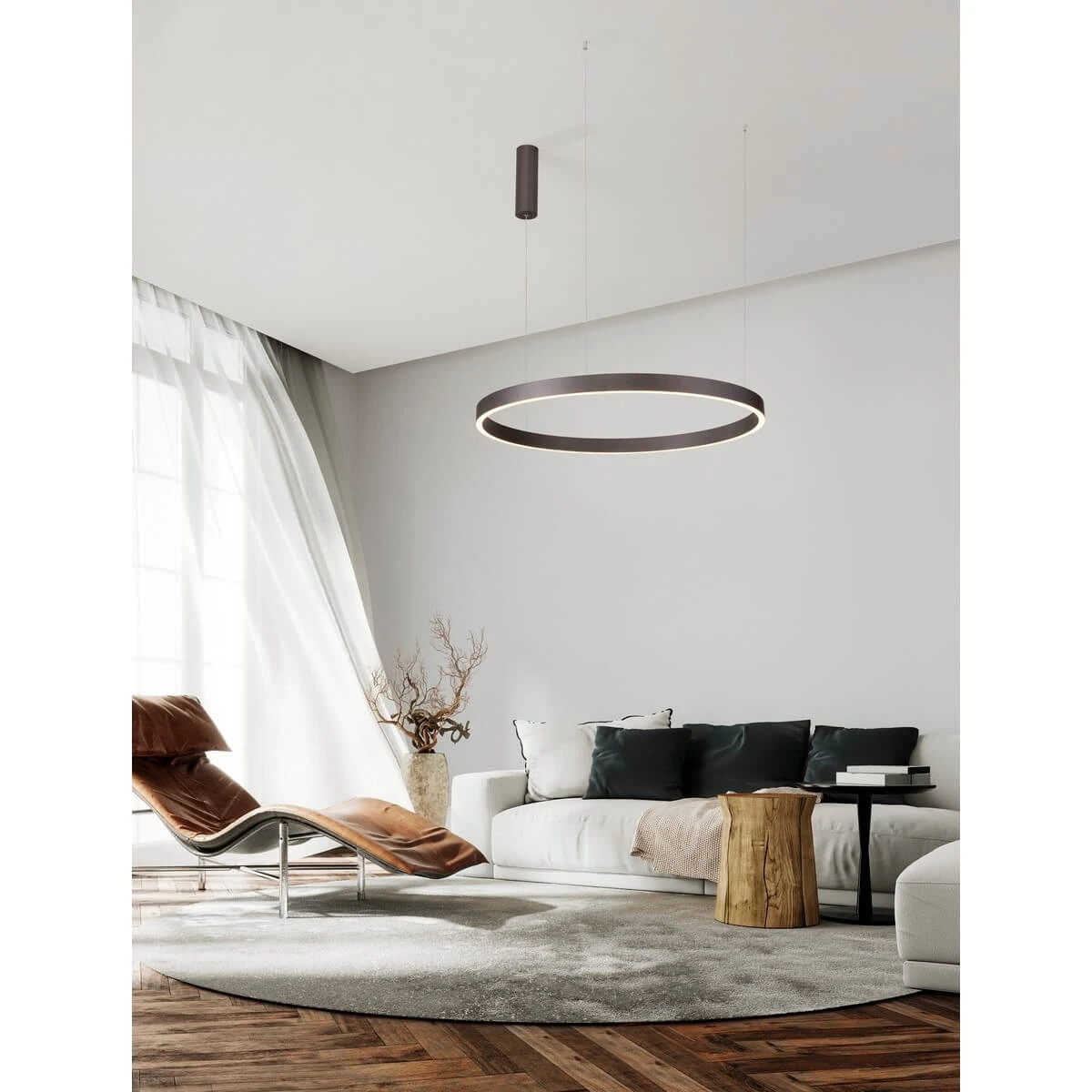 Brązowa lampa wisząca Bari D80 z jednym źródłem LED 77W, zawieszona na cienkich linkach, w kształcie okręgu. Otoczenie to nowoczesny salon z beżowym dywanem, skórzanym fotelem oraz sofy z poduszkami. Tło to jasna ściana z dużymi oknami.