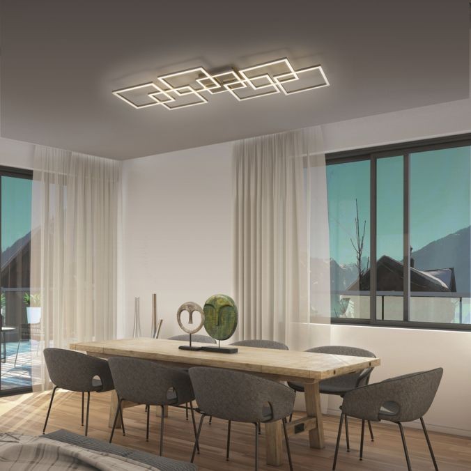 Lampa sufitowa Q-inigo LED 52W CCT w kolorze nikiel satyna, z nowoczesnym, geometrycznym designem. Zainstalowana na suficie w jasnym wnętrzu, z dużymi oknami i drewnianym stołem, tworzy elegancką aranżację.