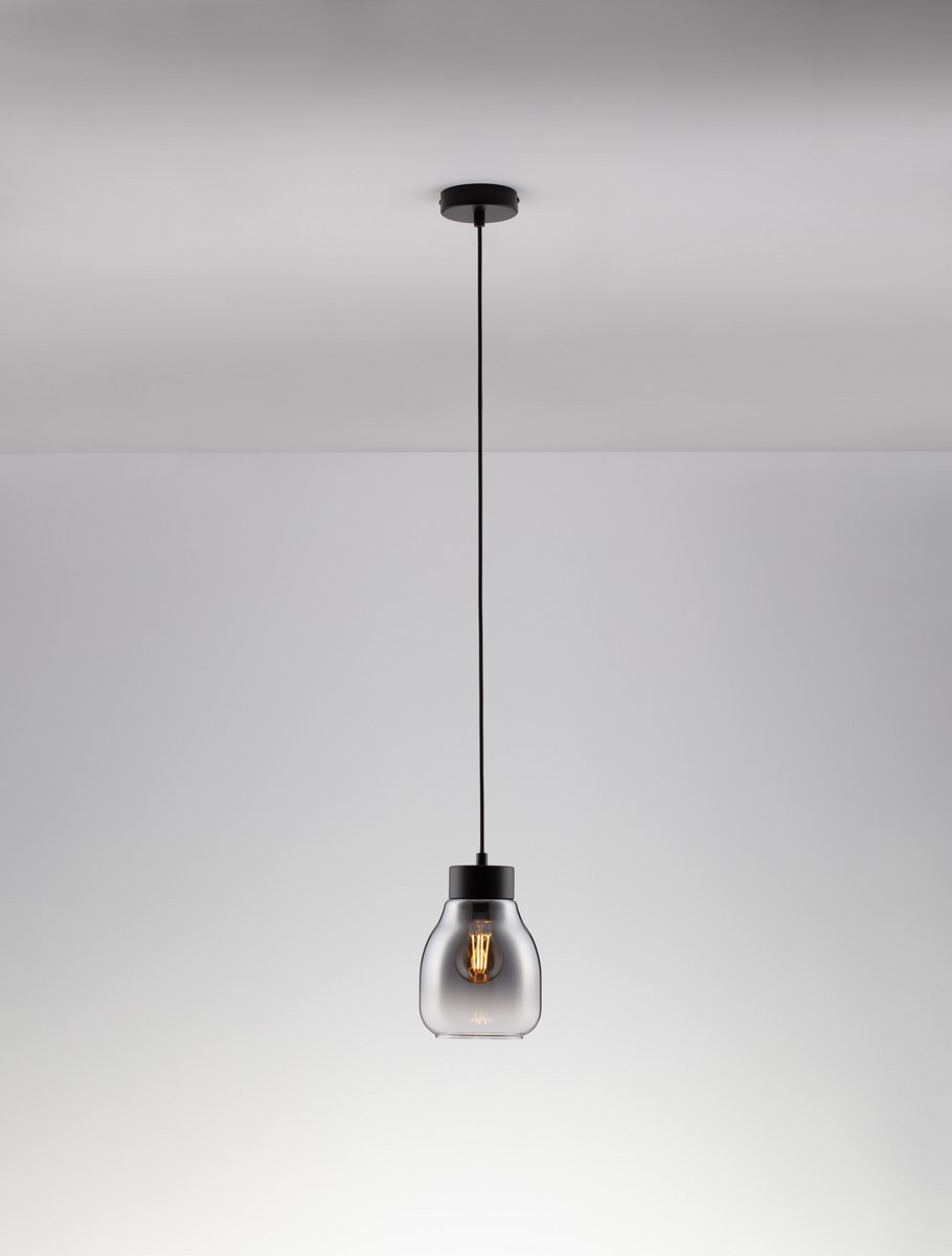 Czarna lampa wisząca Moche z oprawą na żarówkę E27. Szklany klosz w kształcie dzwonu, przezroczysty, z widoczną żarówką wewnątrz. Zawieszona na cienkim, czarnym kablu, montowana do sufitu. Proste tło w jasnych odcieniach.