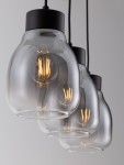 Lampa wisząca Moche z trzema kloszami, w kolorze czarnym, z przezroczystym szkłem. E27, widoczne żarówki. Ujęcie z przodu, klosze w kształcie kulistym, zawieszone na czarnych linkach. Tło jasne, minimalistyczne.