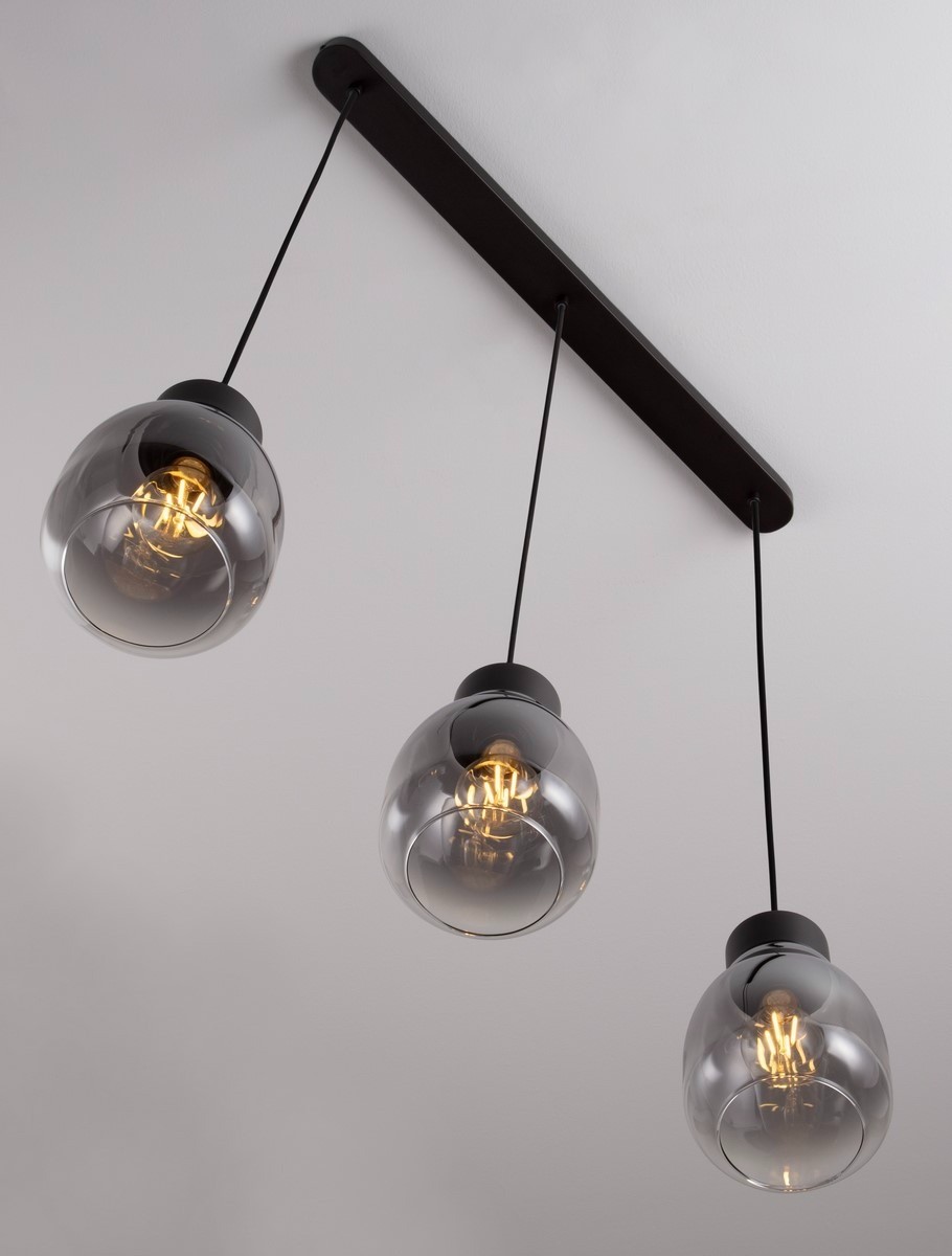 Lampa wisząca Moche z trzema kloszami w kształcie kul, wykonana z przezroczystego szkła w odcieniu szaro-czarnym. Montaż na czarnej, prostokątnej podstawie, zwisająca na cienkich czarnych przewodach. Oświetlenie E27, nowoczesny design.