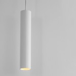Lampa wisząca Nazca w białym kolorze, cylindryczny kształt z teksturowaną powierzchnią. Umieszczona w pionie, z widocznym źródłem światła na dole. Tło w odcieniu szarości, minimalistyczne i neutralne. Idealna do nowoczesnych wnętrz.
