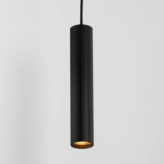 Lampa wisząca Nazca w kolorze czarnym, o cylindrycznym kształcie, z metalowym wykończeniem. Zawieszona na cienkim przewodzie, z widocznym źródłem światła GU10 u dołu. Tło w jasnym kolorze, podkreślające minimalistyczny design.