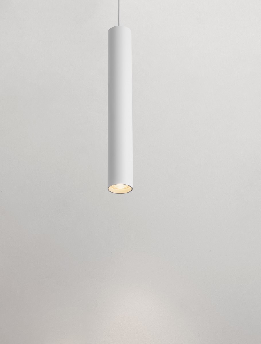 Lampa wisząca Nazca w kolorze białym, o cylindrycznym kształcie, z jedną oprawą na żarówkę GU10. Zawieszona na cienkim kablu, z widocznym źródłem światła na dole. Tło w jasnym kolorze, minimalistyczny design.
