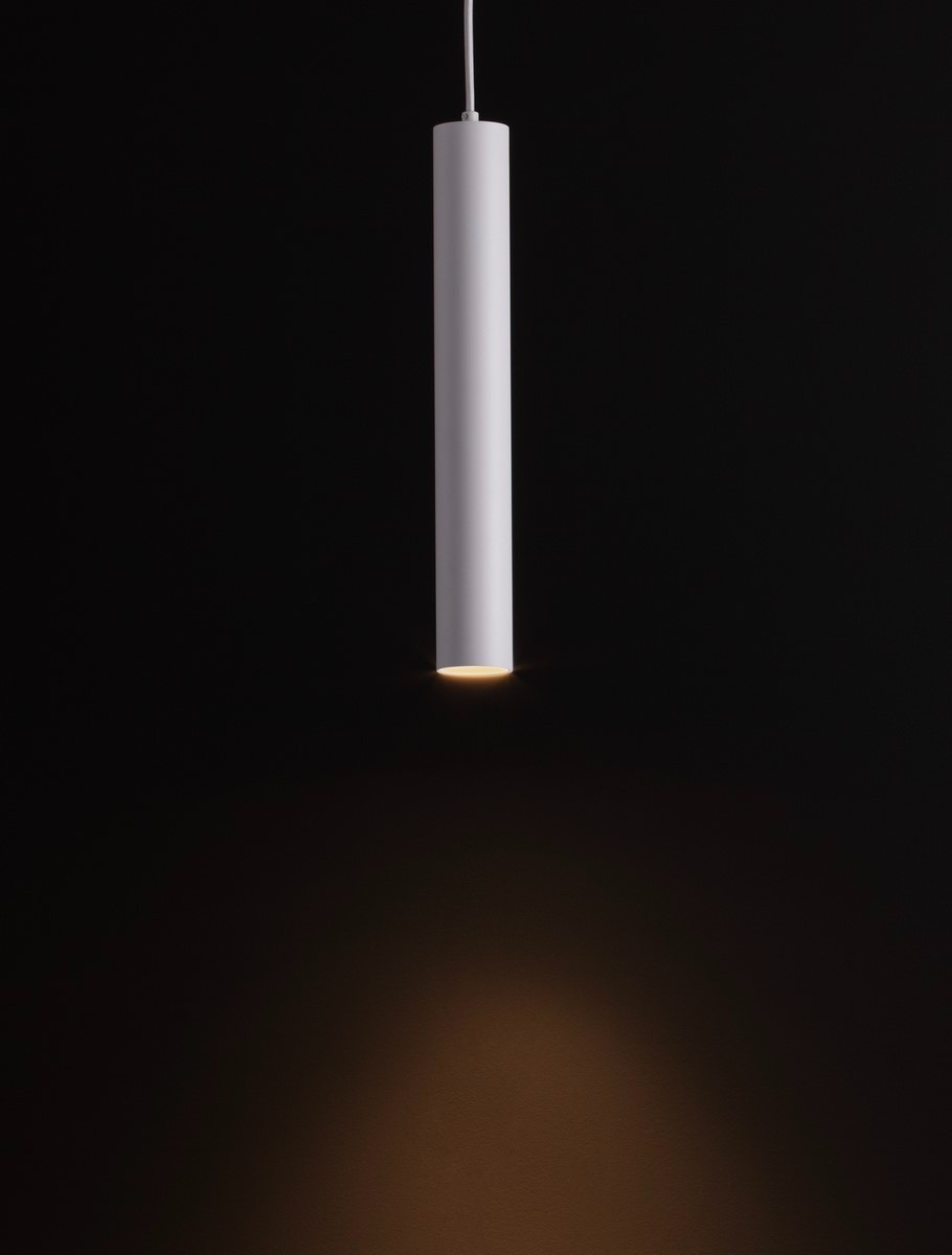 Lampa wisząca Nazca w kolorze białym, o cylindrycznym kształcie, zawieszona na cienkim przewodzie. Emituje światło skierowane w dół, z widocznym miejscem na żarówkę GU10. Tło ciemne, podkreślające minimalistyczny design lampy.