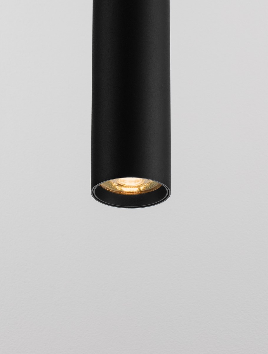 Czarna lampa wisząca Nazca z oprawą na jedną żarówkę GU10, w kształcie cylindrycznym. Ujęcie z dołu, ukazujące szczegóły wnętrza klosza oraz źródło światła. Tło w jasnym kolorze, podkreślające minimalistyczny design produktu.