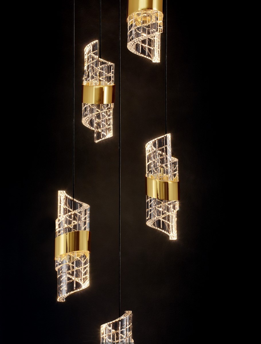 Lampa wisząca Paita z pięcioma źródłami LED, o mocy 41W, w kolorze czarnym. Elementy szklane w kształcie spirali ozdobione złotymi obręczami. Produkt zawieszony na cienkich linkach, na tle ciemnej powierzchni.