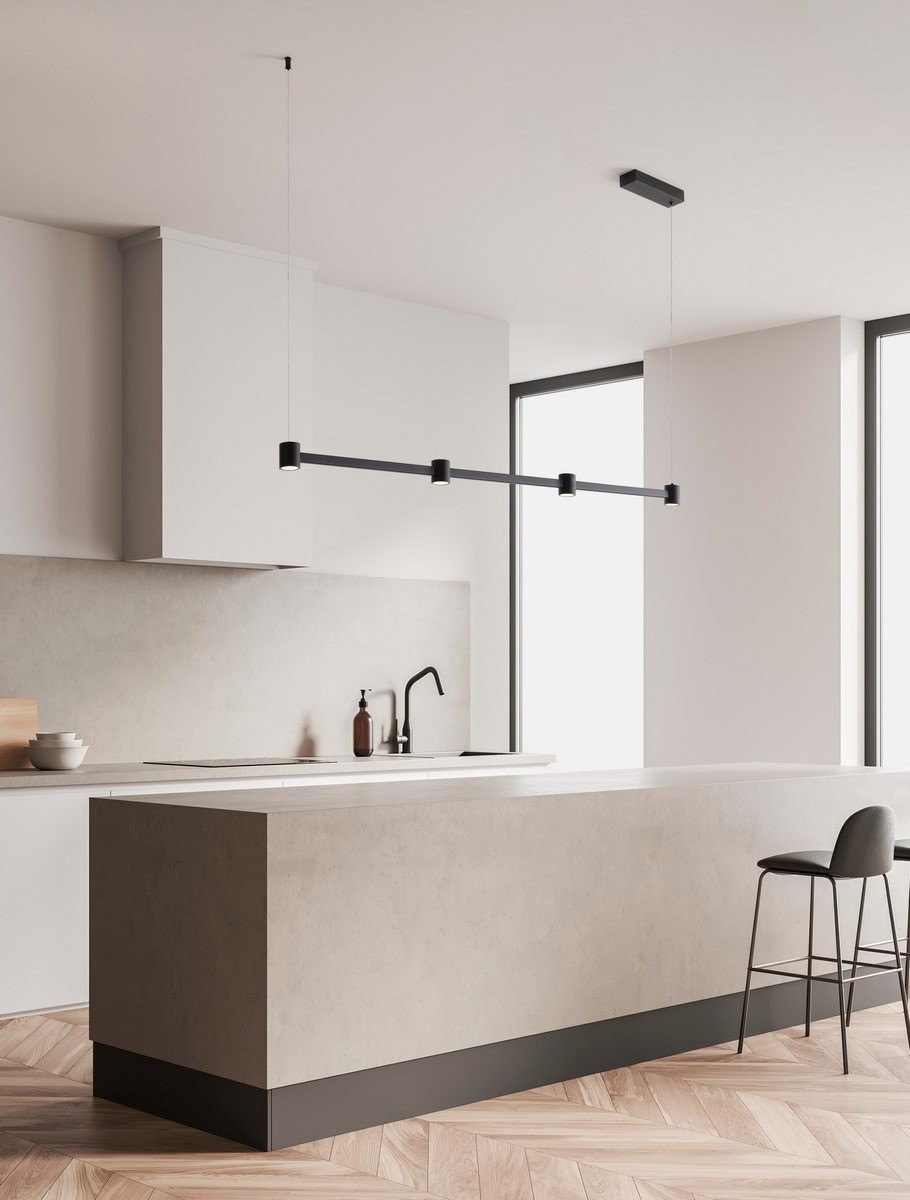 Lampa wisząca Pisco 4xLED 24W w kolorze czarnym, umiejscowiona nad kuchenną wyspą. Prosta konstrukcja z czterema źródłami światła, zawieszona na cienkich linkach. Tło jasne, nowoczesne wnętrze z oknami i minimalistycznymi meblami.
