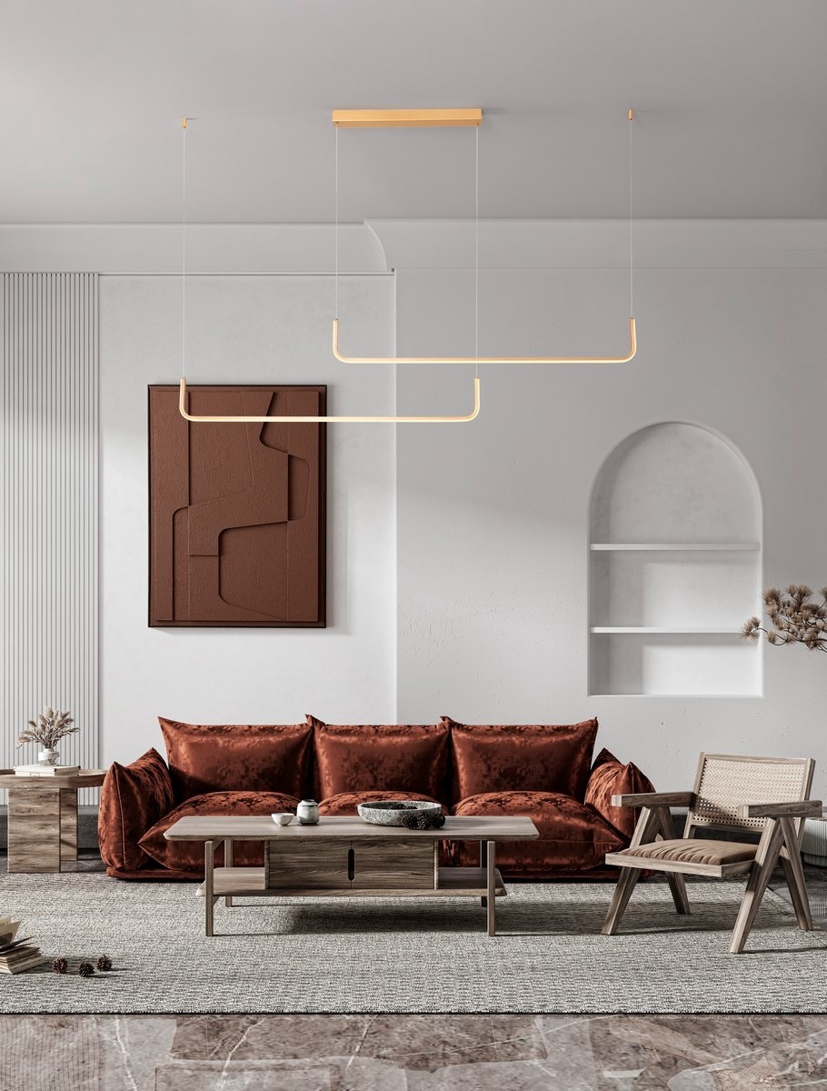 Lampa wisząca Piura z dwoma źródłami LED 40W w kolorze złotym, zawieszona na cienkich linkach. Prosta konstrukcja w kształcie prostokąta, umieszczona w nowoczesnym wnętrzu z brązową sofą oraz minimalistycznymi meblami.