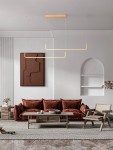 Lampa wisząca Piura z dwoma źródłami LED 40W w kolorze złotym, zawieszona na cienkich linkach. Prosta konstrukcja w kształcie prostokąta, umieszczona w nowoczesnym wnętrzu z brązową sofą oraz minimalistycznymi meblami.