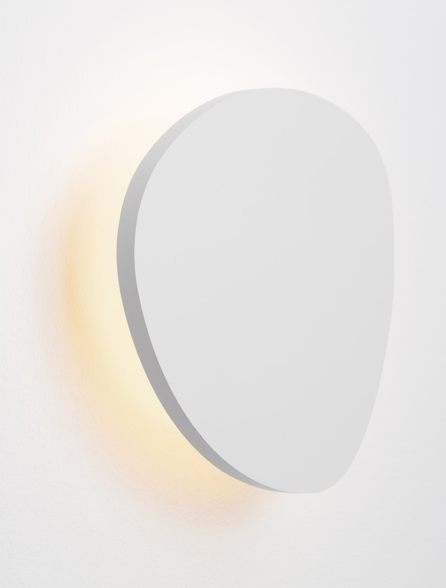 Kinkiet Apure 1xLED 6W w kolorze białym, o owalnym kształcie. Zamontowany na ścianie, emituje ciepłe światło wokół krawędzi. Gładka, matowa powierzchnia bez widocznych napisów czy logo.