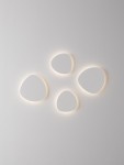 Kinkiet Apure 1xLED 12W w białym kolorze, złożony z czterech nieregularnych kształtów, emitujący przyjemne ciepłe światło. Montowany na ścianie, z minimalistycznym designem, w subtelnym otoczeniu na jasnym tle.