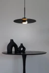 Lampa wisząca Charlie M w kolorze czarnym z oprawą na żarówkę GX53. Posiada okrągły klosz, zawieszona na cienkim przewodzie nad czarnym okrągłym stolikiem, na którym znajdują się trzy czarne wazony o różnych kształtach. Tło w jasnym kolorze.