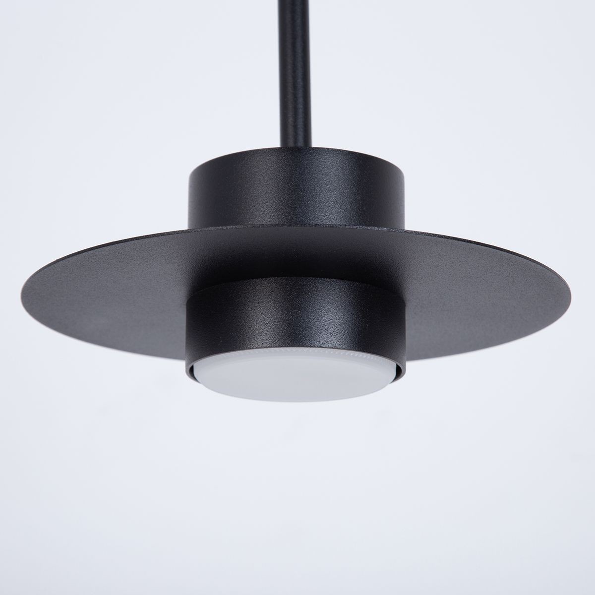 Lampa wisząca Charlie S w kolorze czarnym, z okrągłym kloszem i płaskim daszkiem. Wykonana z metalu, zawieszona na cienkim, prostym kabelku. Widoczna oprawa na żarówkę GX53 w białym kolorze. Ujęcie w zbliżeniu, z góry.