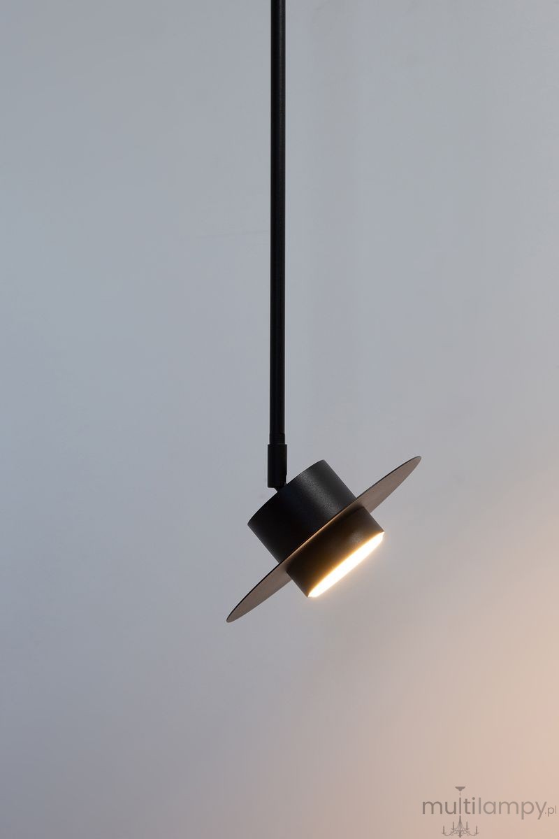Lampa wisząca Charlie M w kolorze czarnym, z jedną oprawą GX53. Ujęcie z boku, ukazujące cylindryczną podstawę z szerokim kloszem. Produkt wisi na cienkim przewodzie, emitując skoncentrowane światło. Tło jednolite, jasne.