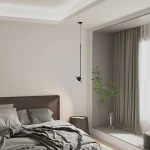 Lampa wisząca Charlie M w kolorze czarnym, z jednym gniazdem GX53, zawieszona na długim przewodzie. Ujęcie z boku, w kontekście sypialni z łóżkiem i rośliną w wazonie. Minimalistyczny design, nowoczesna aranżacja wnętrza.
