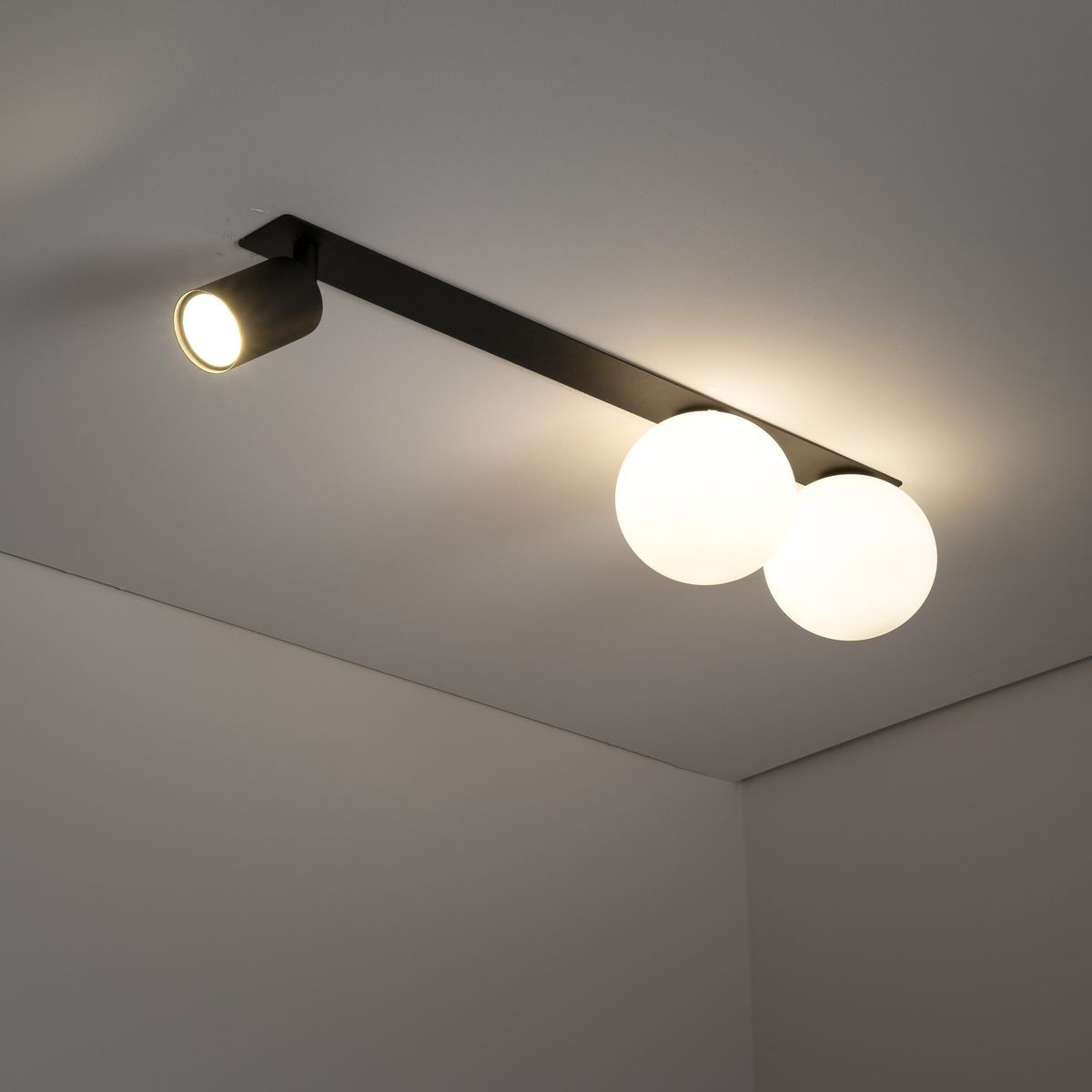 Lampa sufitowa podtynkowa Vox w kolorze czarnym, z jedną oprawą GU10 oraz dwiema oprawami G9. Ułożona poziomo, z dwoma kulistymi kloszami i jednym reflektorem, emitującym ciepłe światło na jasnym tle sufitu.