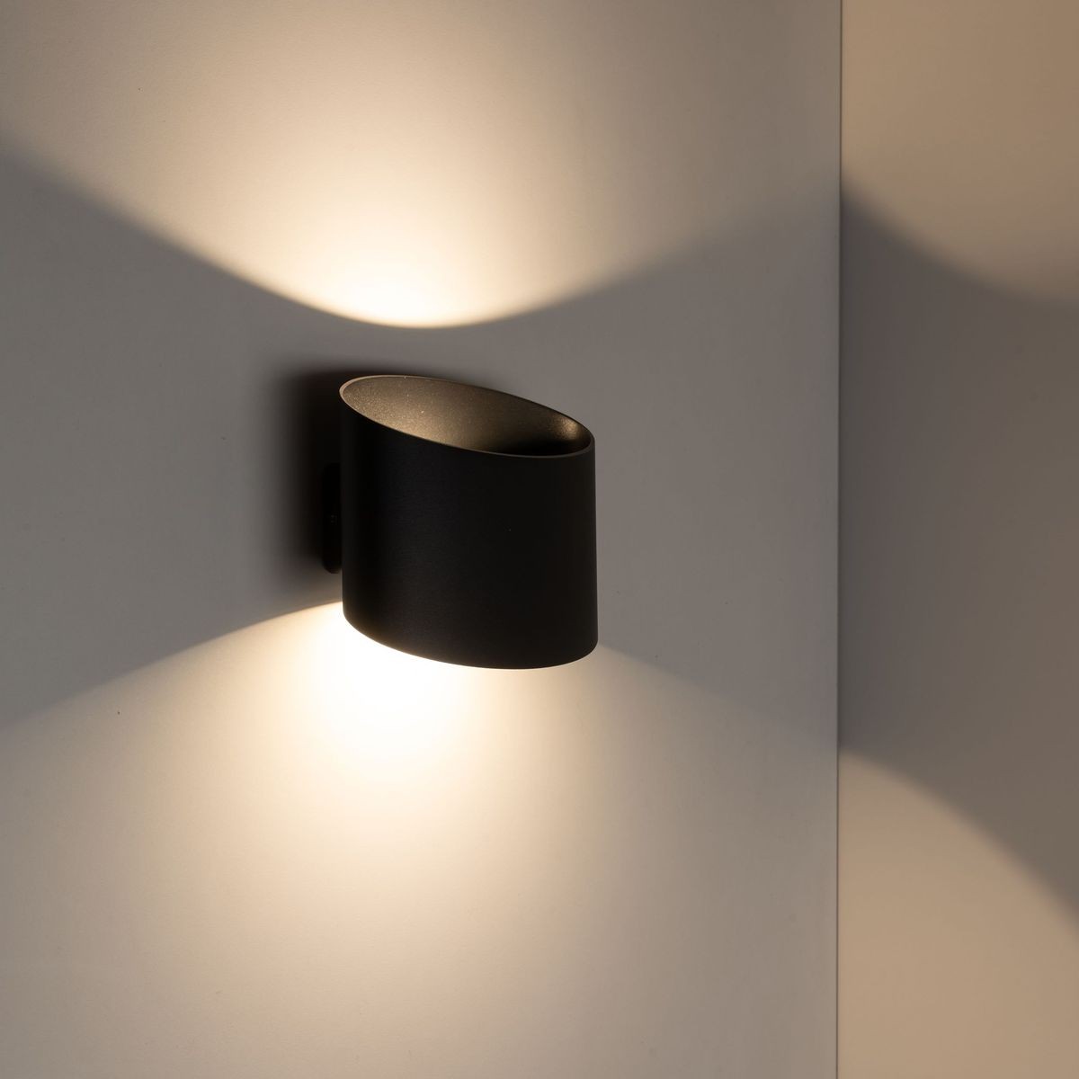 Kinkiet Verto 1xLED 22W IP54 w kolorze czarnym, zamontowany na ścianie, o cylindrycznym kształcie. Emituje ciepłe światło, tworząc na ścianie delikatne cienie. Wykonany z materiału odpornego na wilgoć.