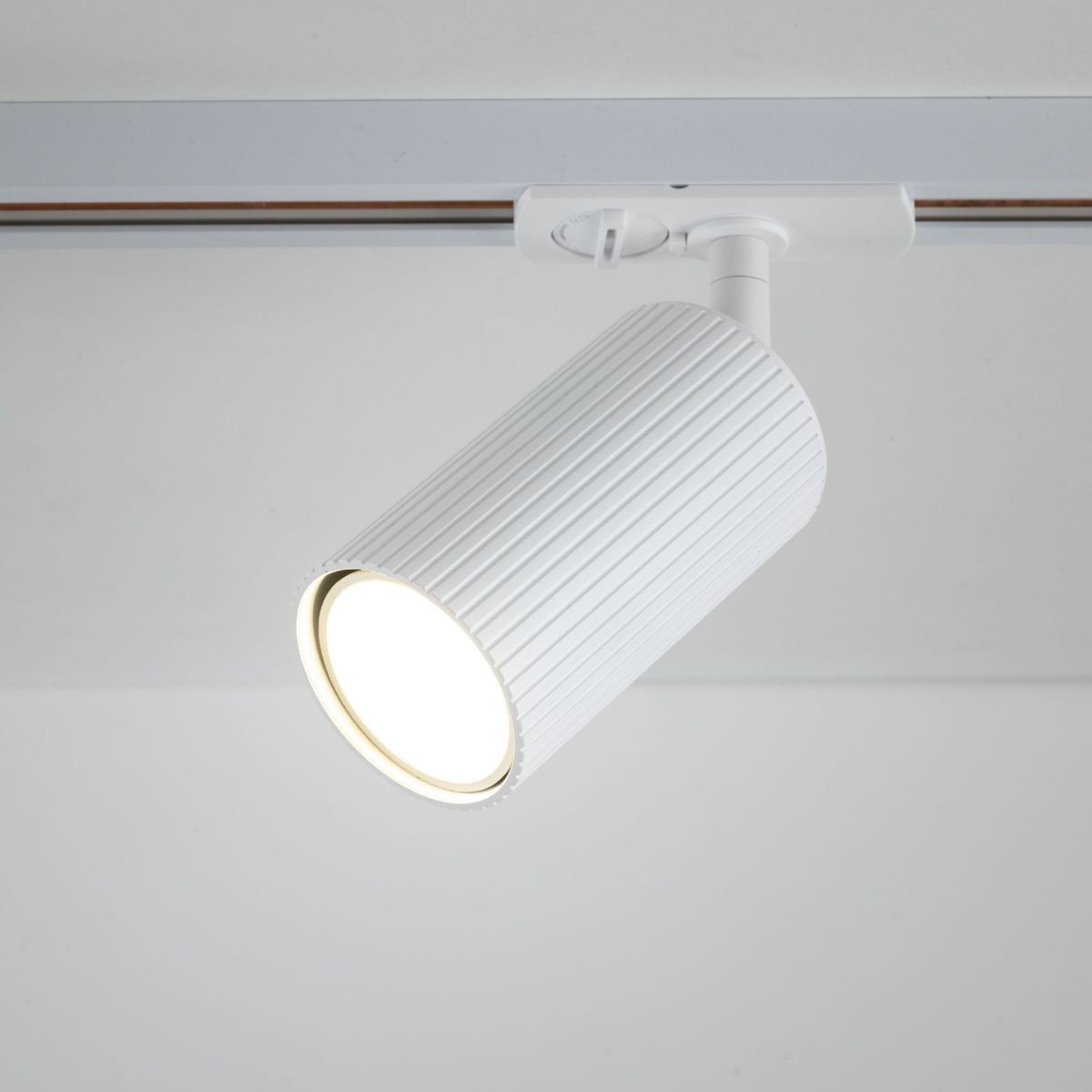 Reflektor spot Tracer Tune 1xGU10 w kolorze białym, zamontowany na szynie. Posiada cylindryczny kształt z wyżłobieniami na powierzchni oraz otwór emitujący światło. Ujęcie z góry, zbliżenie na detal lampy.