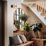 Kinkiet Estera 1xG9 w brązowej oprawie z bursztynowym kloszem, zamontowany na ścianie obok okrągłego lustra. W tle widoczne rośliny doniczkowe oraz drewniana półka. Oświetlenie tworzy przytulną atmosferę w aranżacji wnętrza.