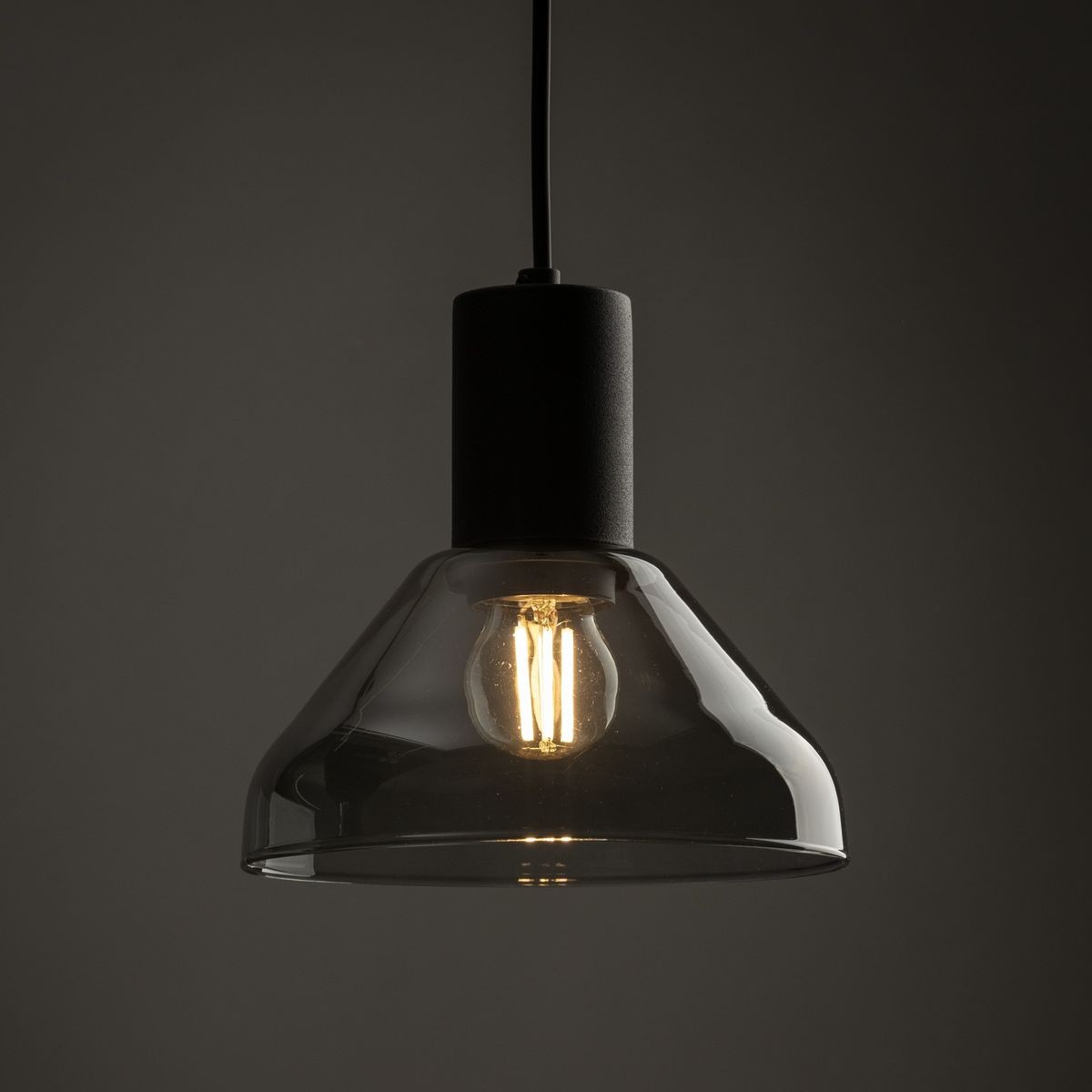 Lampa wisząca Tracer Neo z oprawą w kolorze czarnym, z kloszem w odcieniu grafitowym. Zawiera żarówkę E27, wisi na cienkim przewodzie. Klosz ma kształt stożkowy, przezroczysty, z widoczną żarówką, co podkreśla industrialny styl.