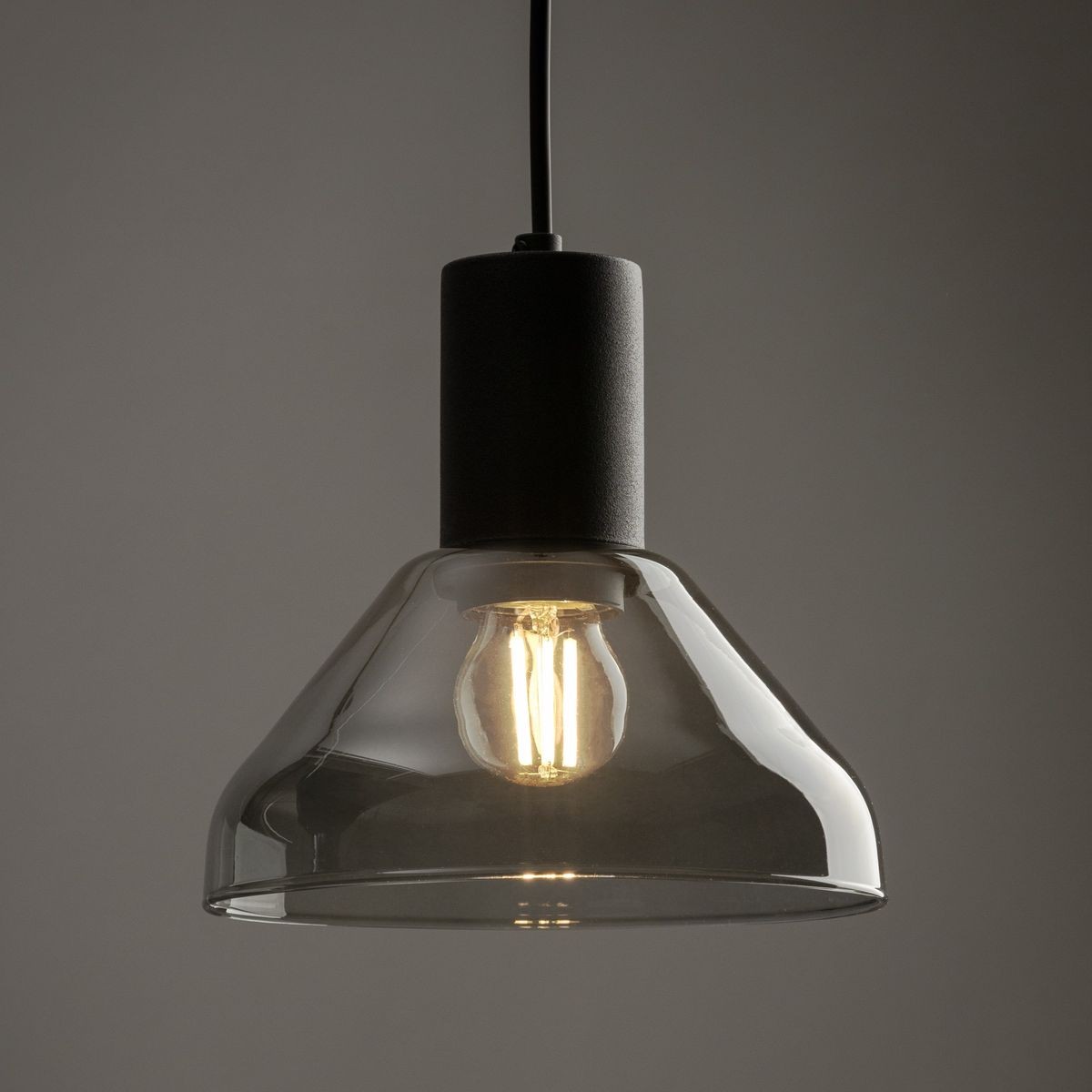 Lampa wisząca Tracer Neo w kolorze czarnym z grafitowym wykończeniem, z kloszem w kształcie dzwonu z przezroczystego szkła. Widoczna żarówka E27, zawieszona na cienkim przewodzie. Kąt ujęcia zbliżenie na detal. Tło szare, minimalistyczne.