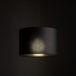 Lampa wisząca Tracer D30 w kolorze czarnym, z okrągłym abażurem z tkaniny. Ujęcie z góry pokazuje lampa zawieszoną na cienkim przewodzie, z widocznym światłem emitowanym przez dolną część abażura. Tło ciemne, minimalistyczne.