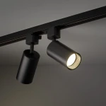Reflektor spot Tracer Amis 1xGU10 w kolorze czarnym, zamontowany na szynie. Zbliżenie na cylindryczny kształt oprawy z widoczną żarówką, emitującą ciepłe światło. Produkt w nowoczesnym stylu, idealny do oświetlenia wnętrz.