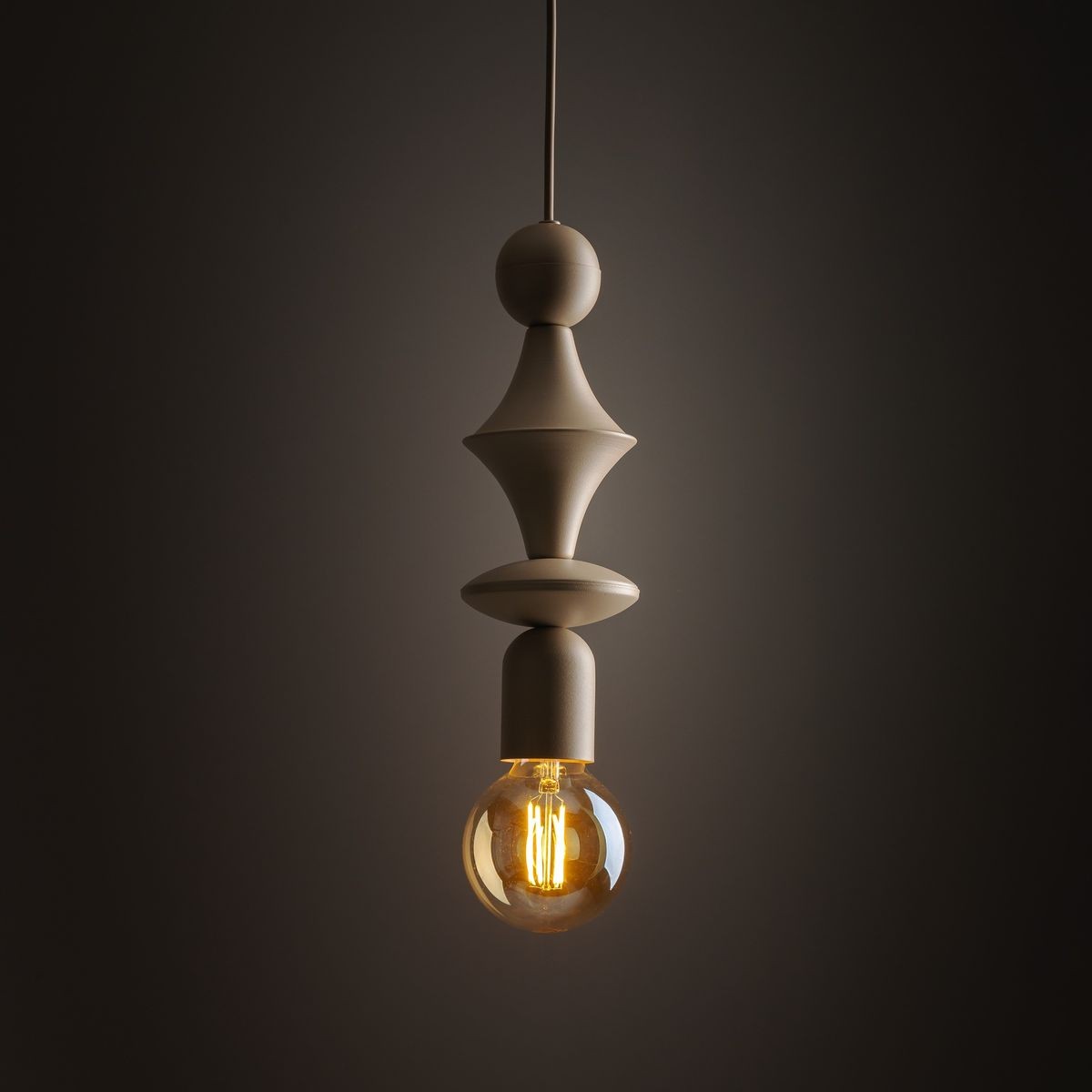 Beżowa lampa wisząca Tower z oprawą na żarówkę E27, o eleganckim, nowoczesnym kształcie z dekoracyjnymi elementami. Zawieszona na cienkim przewodzie, z okrągłym kloszem, emitującym ciepłe światło w przyciemnionym tle.