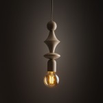 Beżowa lampa wisząca Tower z oprawą na żarówkę E27, o eleganckim, nowoczesnym kształcie z dekoracyjnymi elementami. Zawieszona na cienkim przewodzie, z okrągłym kloszem, emitującym ciepłe światło w przyciemnionym tle.