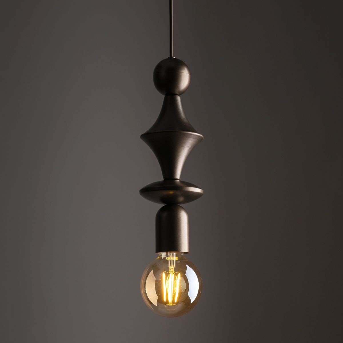 Lampa wisząca Tower w kolorze brązowym z jednym gniazdem E27, o unikalnym kształcie z dekoracyjnymi elementami, zawieszona na cienkim przewodzie, z widoczną żarówką o okrągłym kształcie. Tło ciemne, podkreślające design lampy.