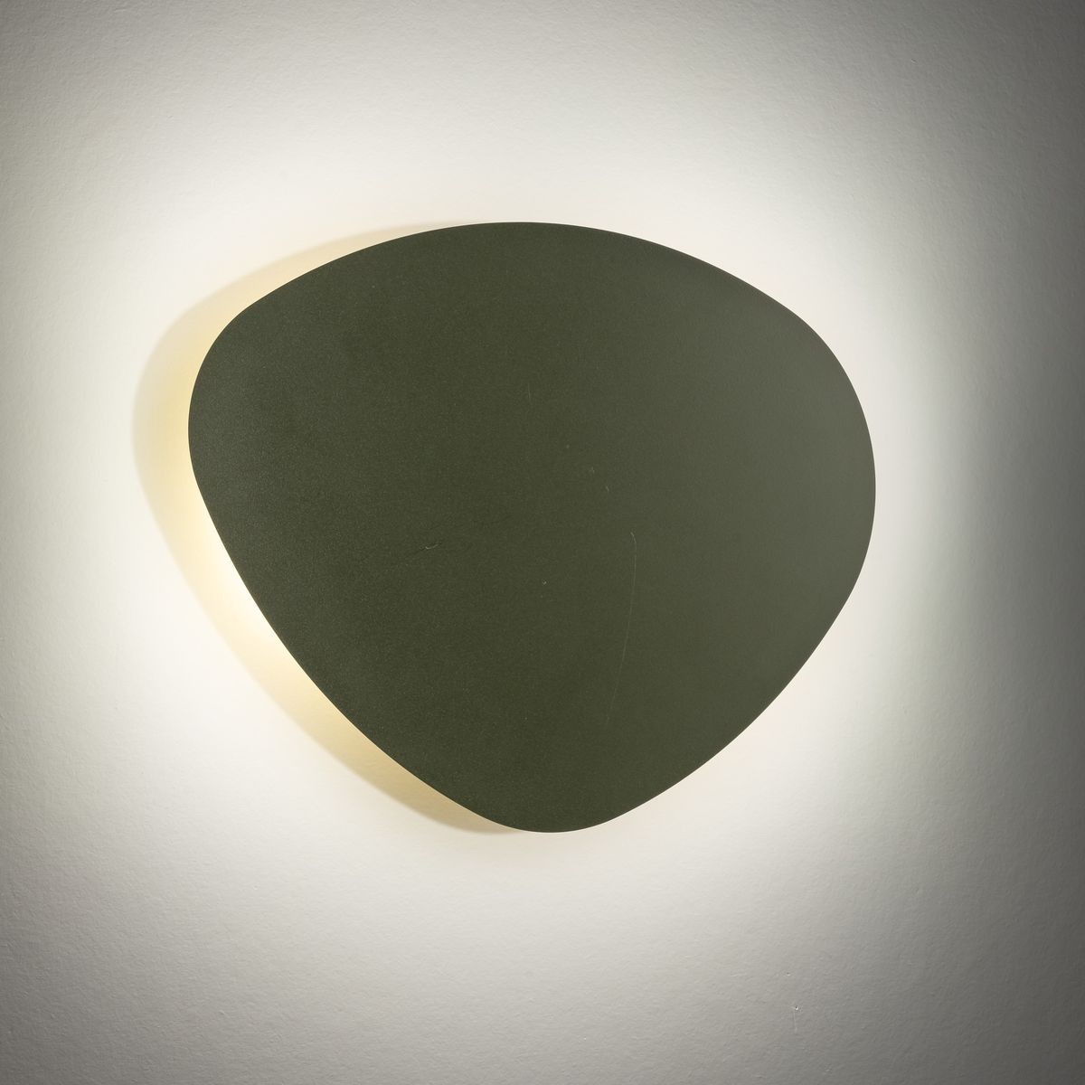 Kinkiet Stone w kolorze zielonym, o nieregularnym kształcie, montowany na ścianie. Emituje ciepłe światło wokół krawędzi, co podkreśla jego nowoczesny design. Używa dwóch żarówek G9. Tło jest jasne, co kontrastuje z ciemniejszym odcieniem lampy.