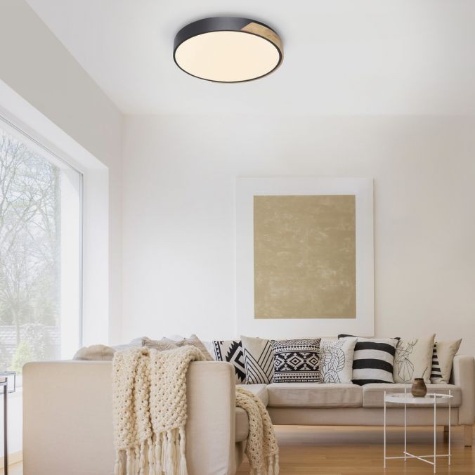 Lampa sufitowa Q-bila LED 35W CCT w kolorze czarnym z drewnianymi akcentami, zamontowana na suficie. Okrągła, z miękkim, rozproszonym światłem, idealna do nowoczesnych wnętrz. W tle widoczny komfortowy salon z kanapą i dekoracyjnymi poduszkami.