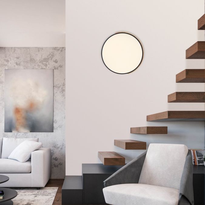 Lampa sufitowa Q-bila LED 35W CCT w kolorze czarnym z drewnianymi akcentami, okrągła, zamontowana na ścianie. W tle widoczny nowoczesny salon z szarym sofą i drewnianymi schodami.