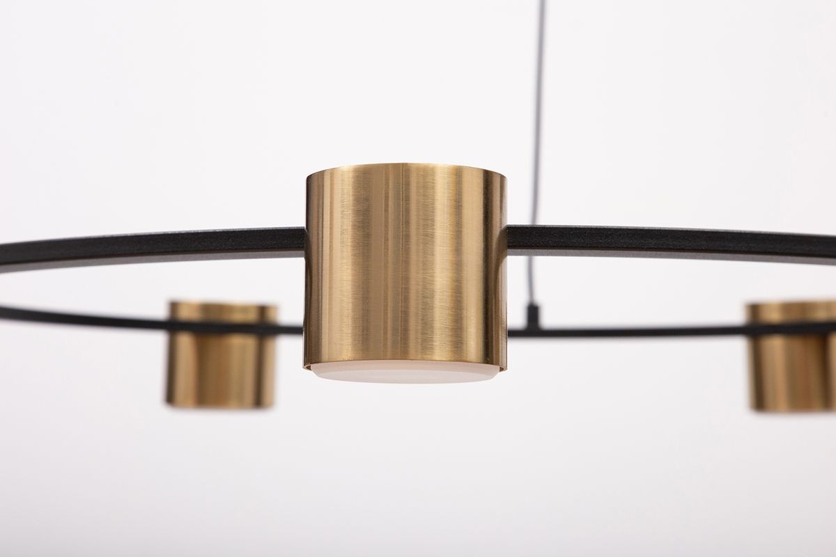 Lampa wisząca Kodo w kolorze czarnym i mosiądzu, z pięcioma uchwytami na żarówki GX53. Widok z bliska na metalowe detale oraz okrągłą, prostą konstrukcję. Tło białe, podkreślające elegancki design.