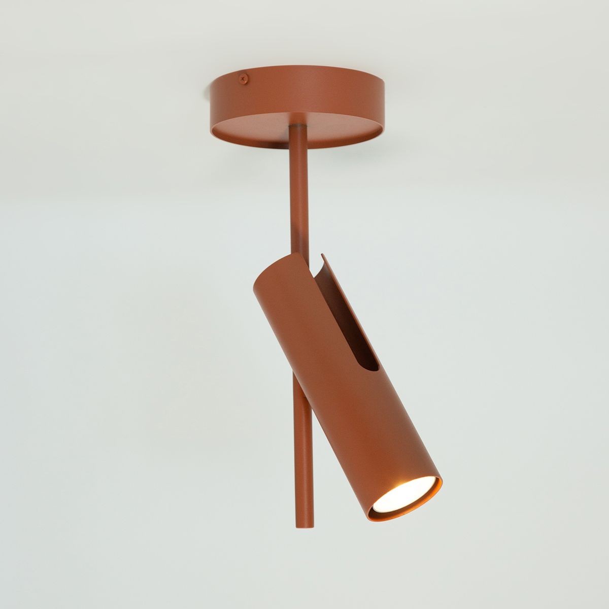 Lampa sufitowa Leda w kolorze ceglastym, z pojedynczym spotem GU10, umieszczona pod kątem. Metalowa konstrukcja z otwartym wlotem, montowana do sufitu, z prostym, minimalistycznym designem.