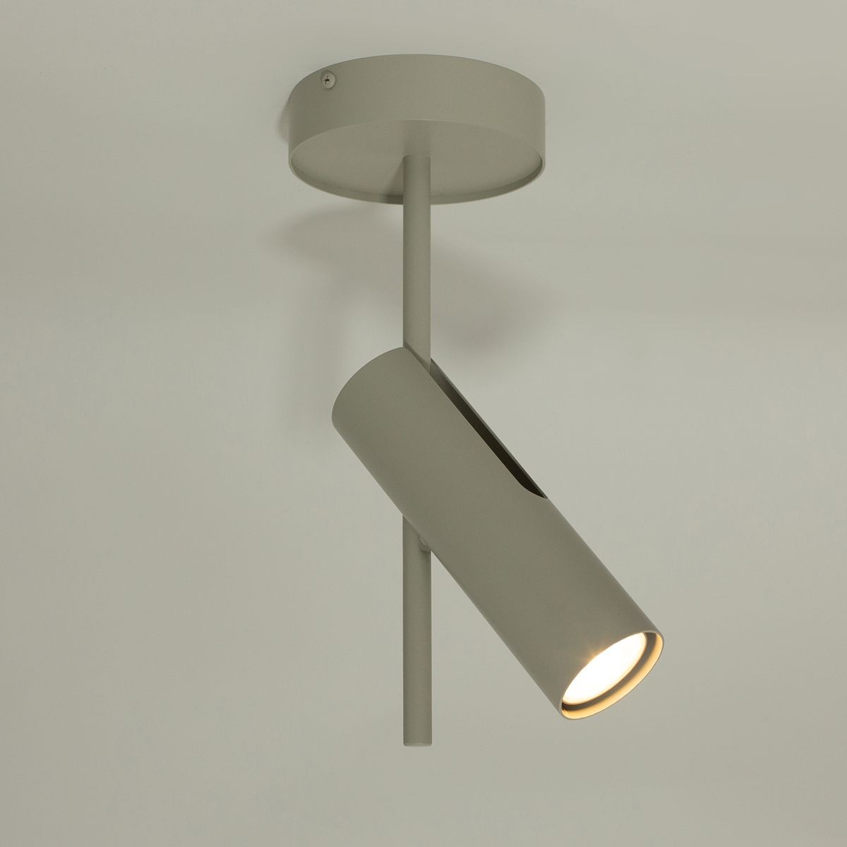 Leda lampa sufitowa typu spot w kolorze szarym beżowym, z jedną oprawą GU10. Ujęcie z dołu, pokazujące cylindryczny kształt lampy oraz mocowanie do sufitu. Lampka skierowana w dół, emitująca światło z jednego źródła.