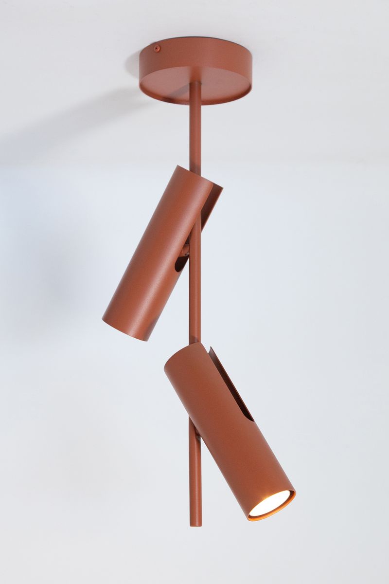 Lampa wisząca Leda w kolorze ceglastym z dwiema regulowanymi oprawami na żarówki GU10. Ujęcie z góry, pokazujące elegancką, cylindryczną formę oraz metalowy stelaż. Produkt zawieszony na suficie, na tle jasnej ściany.
