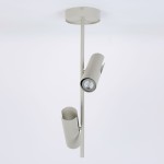 Lampa wisząca Leda w kolorze szarym beżowym z dwoma uchwytami na żarówki GU10. Zawieszona na prostej, metalowej konstrukcji, z efektownym kształtem reflektorów skierowanych w różne strony. Tło białe, minimalistyczne.
