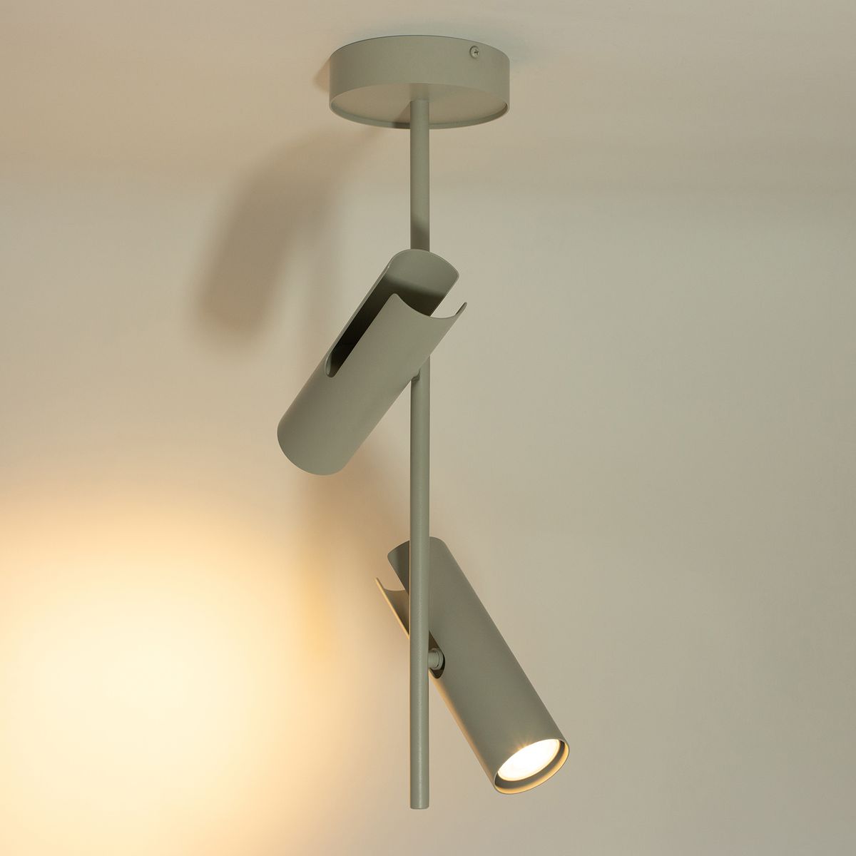 Lampa wisząca Leda z dwoma oprawami GU10 w kolorze szarym beżowym. Wykonana z metalu, z cylindrycznymi kloszami, zawieszona na prostym uchwycie. Ujęcie z dołu, ukazujące detale konstrukcji i źródło światła.