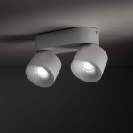 Lampa sufitowa Spark z dwoma reflektorami LED w kolorze białym, umocowana na prostokątnej podstawie. Reflektory mają okrągły kształt i emitują jasne światło. Ujęcie z dołu, pokazujące detale konstrukcji i kąt ustawienia.