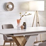 Beżowy kinkiet Slate z jedną żarówką G9, montowany na ścianie, okrągła metalowa osłona z białym kloszem. W tle widoczny stół z dekoracjami oraz lampa stojąca na trójnogu. Jasne, minimalistyczne wnętrze.