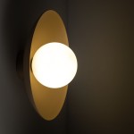 Beżowy kinkiet Slate z okrągłą, matową żarówką o ciepłym świetle, zamontowany na ścianie. Kinkiet ma elegancki, minimalistyczny kształt z dużą, owalną podstawą, tworząc nowoczesny akcent w aranżacji wnętrza.